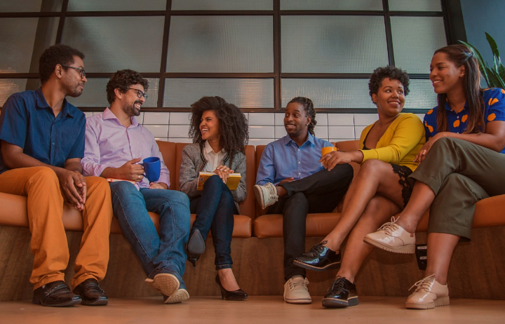 Equipe de seis pessoas sorrindo e discutindo juntos no sofá